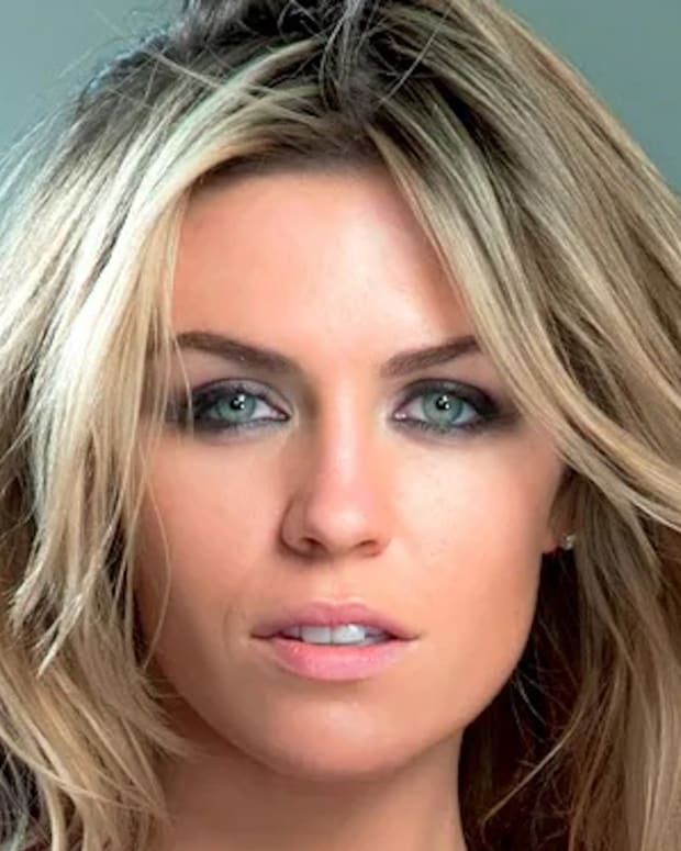 Abigail Clancy poses in front of a gray backdrop and wears her hair in a slight wave.